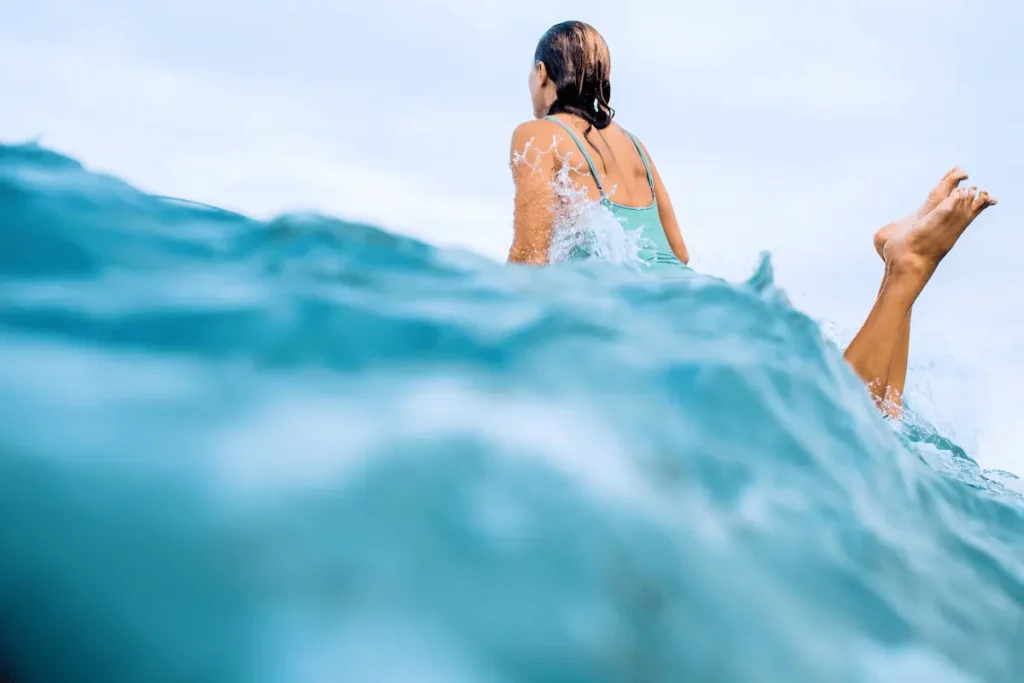 Mulher vista de costas, entra no mar entre ondas azuis, em imagem que remete aos cuidados com os olhos no mar e piscina.